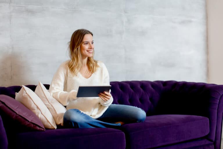 Woman on a sofa holding a tablet and looking into the distance